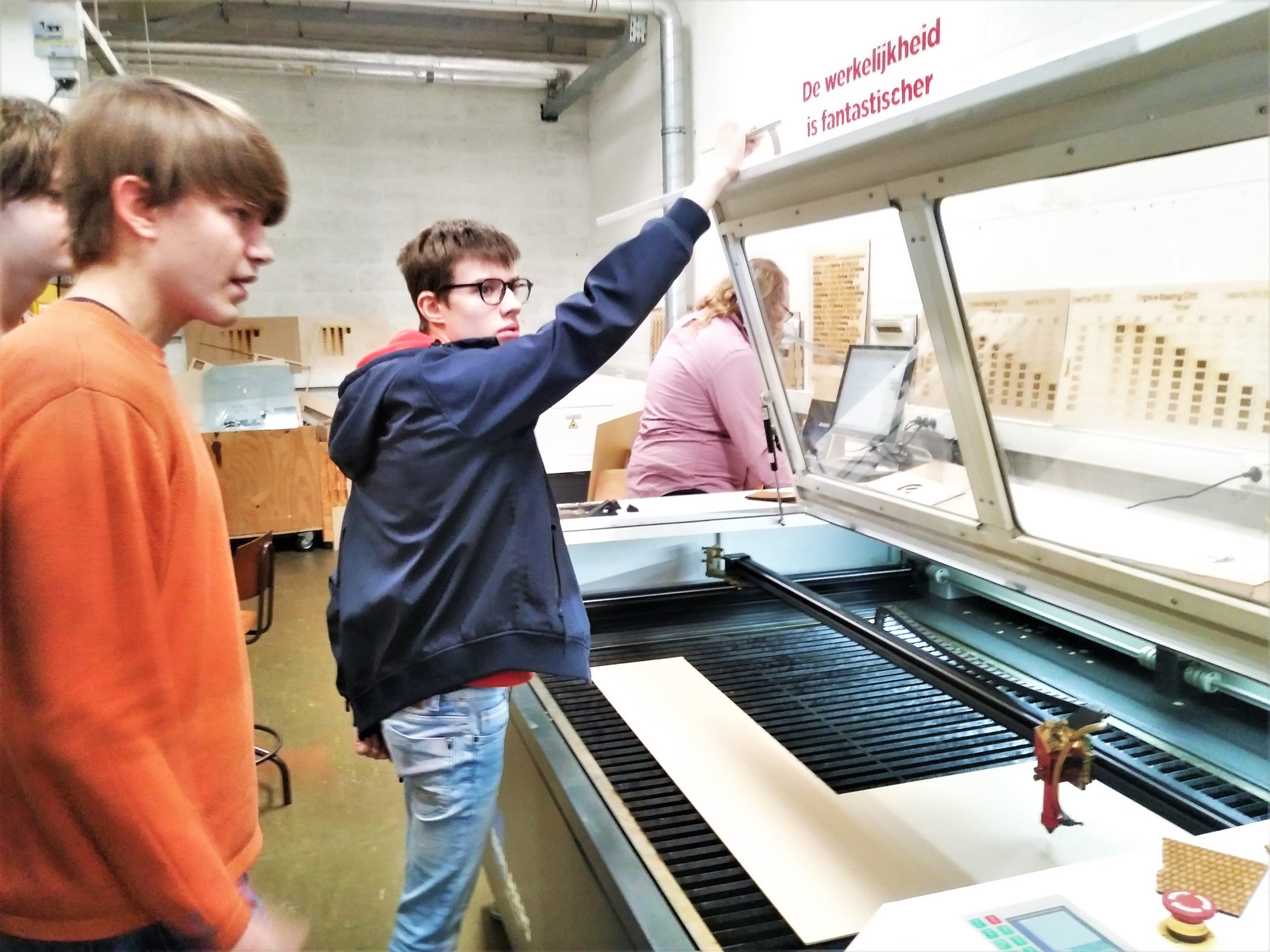 Enkele jongeren gebruiken een machine tijdens een bezoek aan FabLab