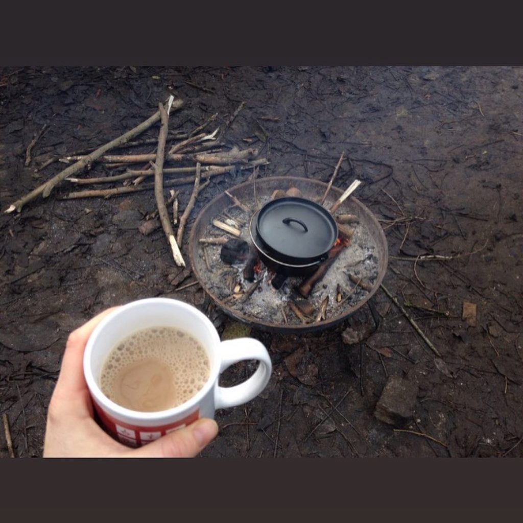 Openlucht koken op vuur en hand met een kopje koffie
