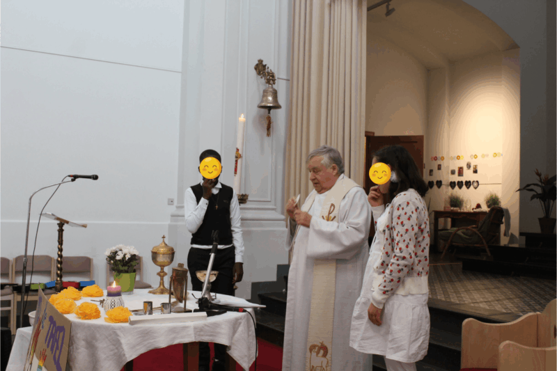 Twee jongeren staan naast aan weerszijden van een priester en eten een hostie tijdens Vormselviering.