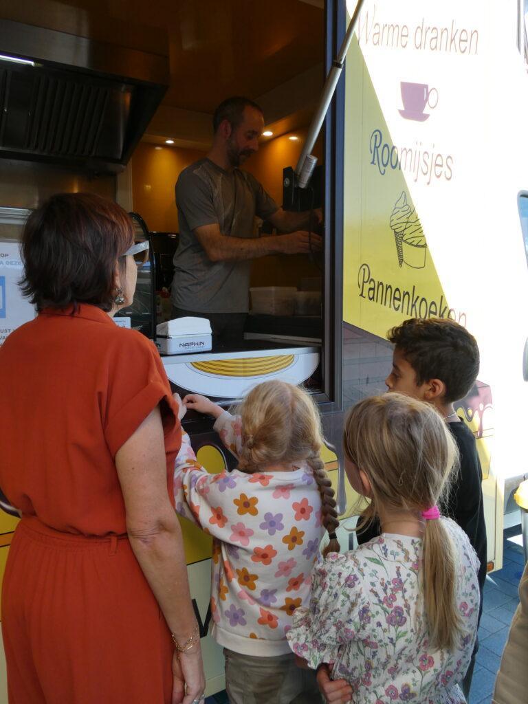 Kinderen en begeleider staan aan te schuiven aan een foodtruck om een pannenkoek te krijgen.